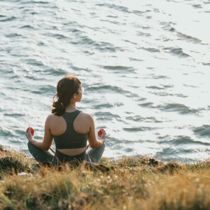 woman sits with her legs crossed facing the ocean